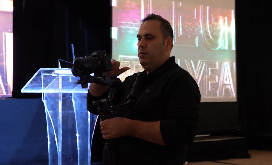 Camera operator holding a Ronin-stabilized camera beside the lectern