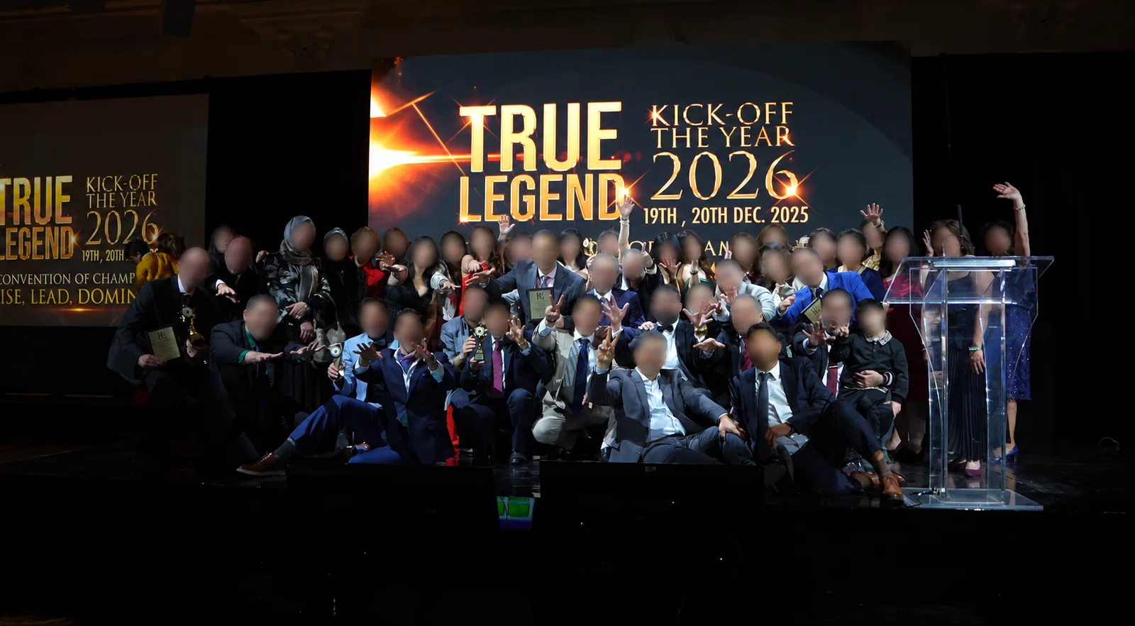 Large group on stage beneath the TRUE LEGEND kickoff screen, faces blurred