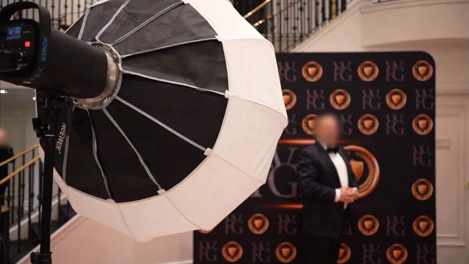 Portrait lighting setup with umbrella light and blurred-face attendee