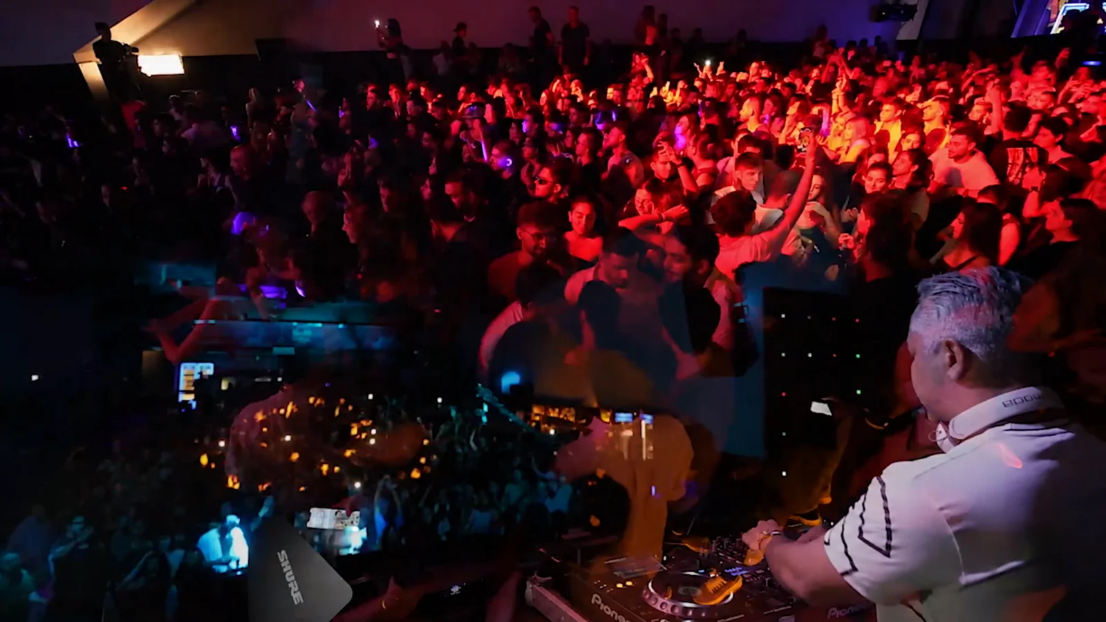 Concert crowd and DJ under red stage lighting
